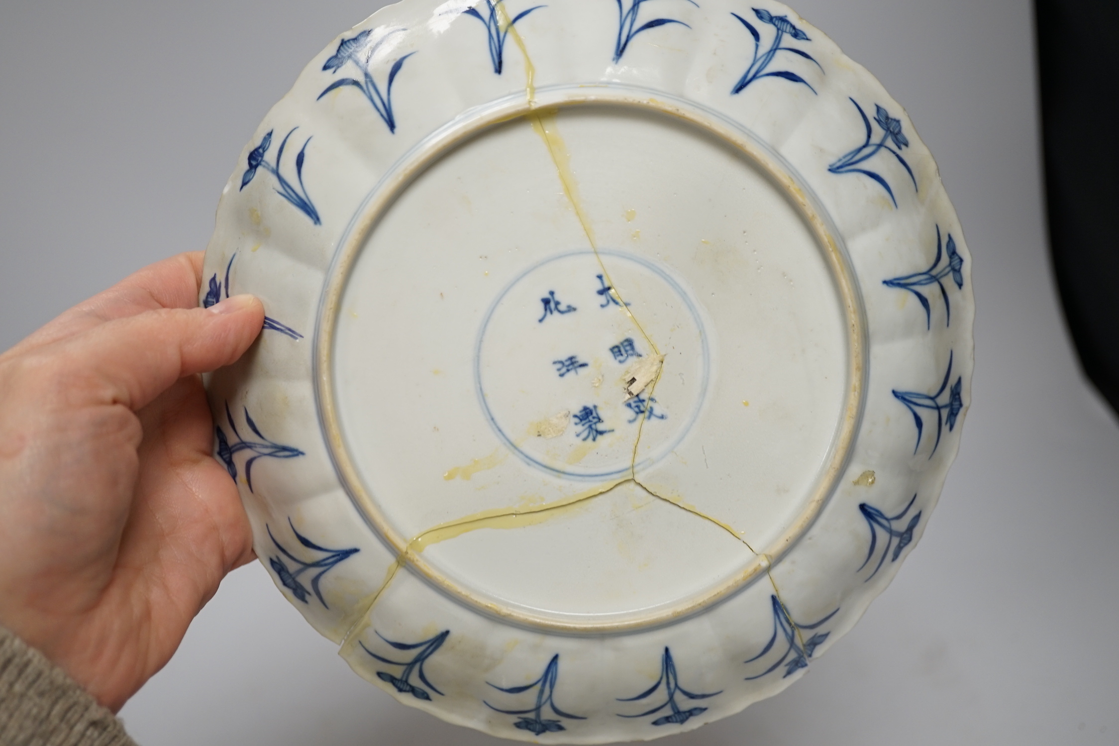 A Chinese blue and white ‘warriors’ bowl, Kangxi mark and period, a similar ‘hunting’ saucer dish, and a famille verte saucer dish, all Kangxi period (3), largest 27cm in diameter